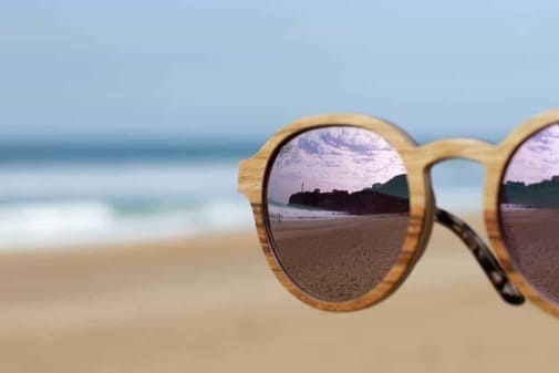lunettes de soleil en bois, verres polarisés et teintés rose reflétant la plage et le phare de Biarritz. 